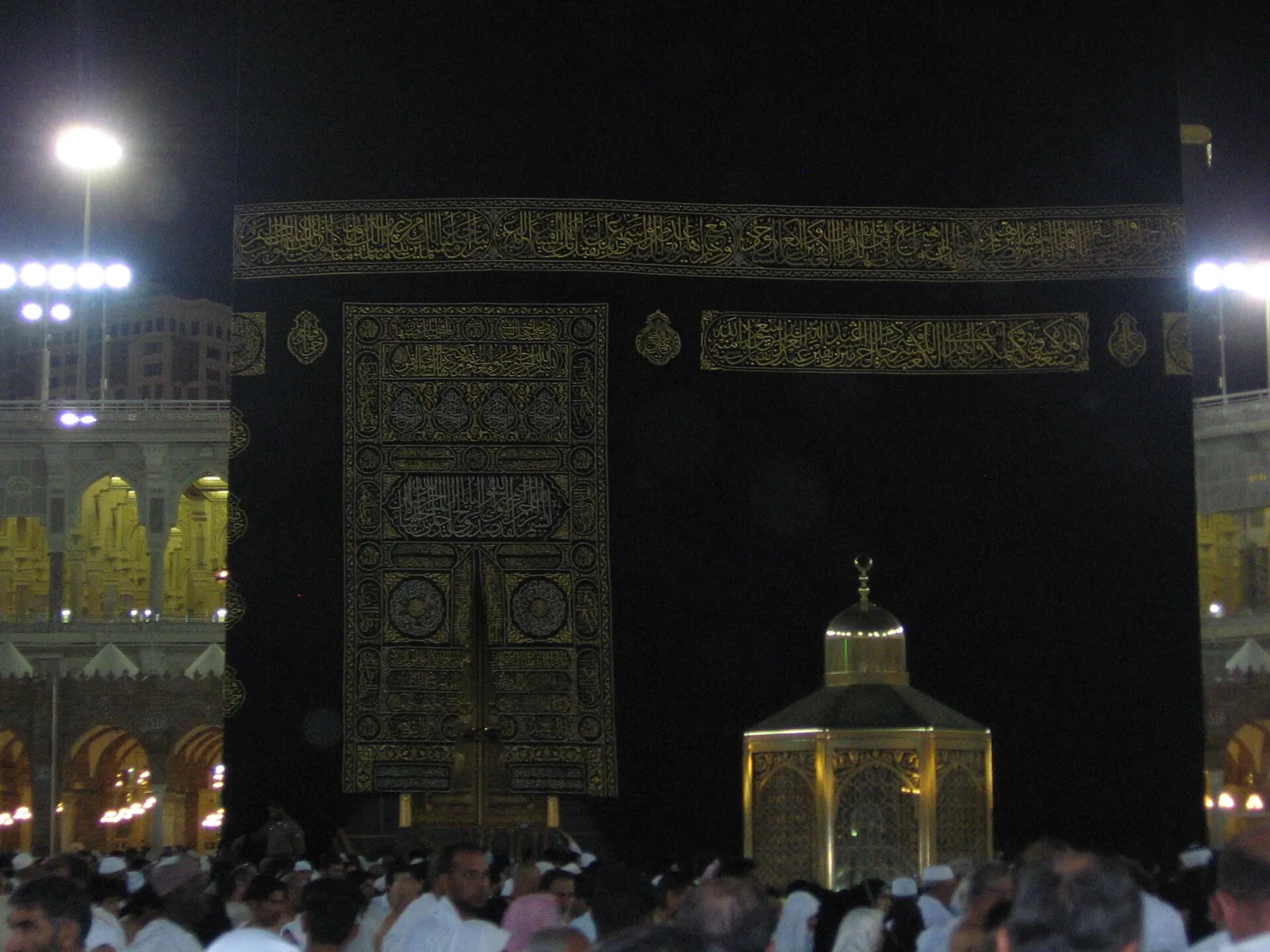 The gold-toned glass enclosure of Maqam Ibrahim standing on the marble floor near the Kaaba